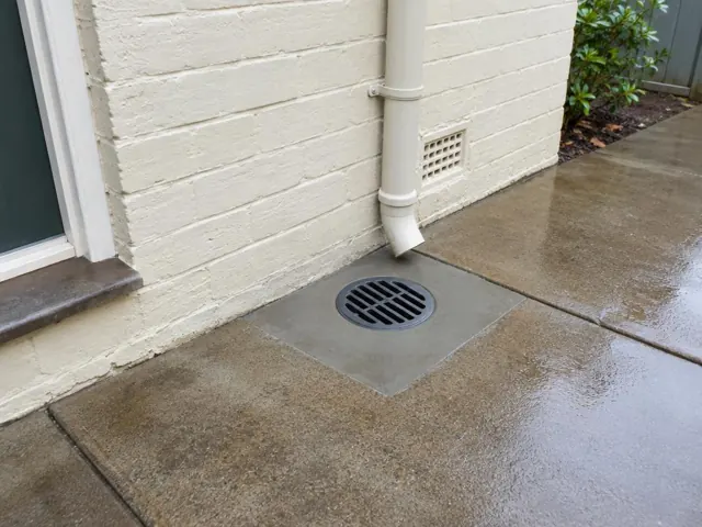 Clean round outdoor drain set in wet concrete paving beside a cream brick wall in North Lambton
