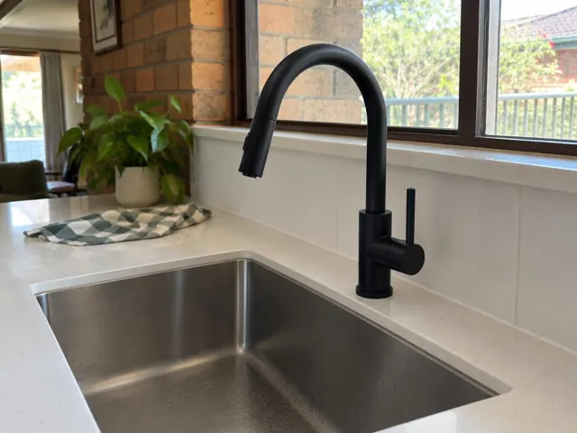 Black kitchen mixer tap above a stainless steel sink with tiled splashback in Callaghan