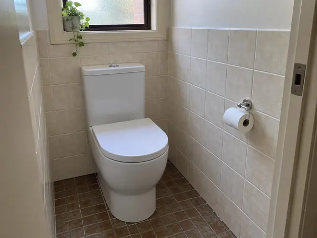 White toilet in a small tiled bathroom with a window and toilet roll holder in Birmingham Gardens